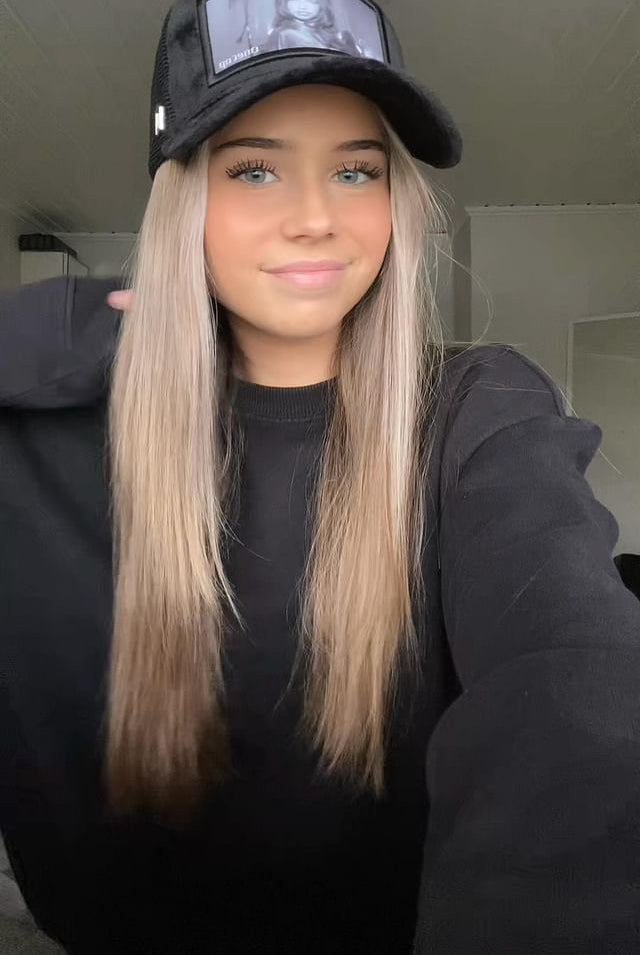Woman with long blond hair wearing a black cap and black sweater smiles while posing indoors