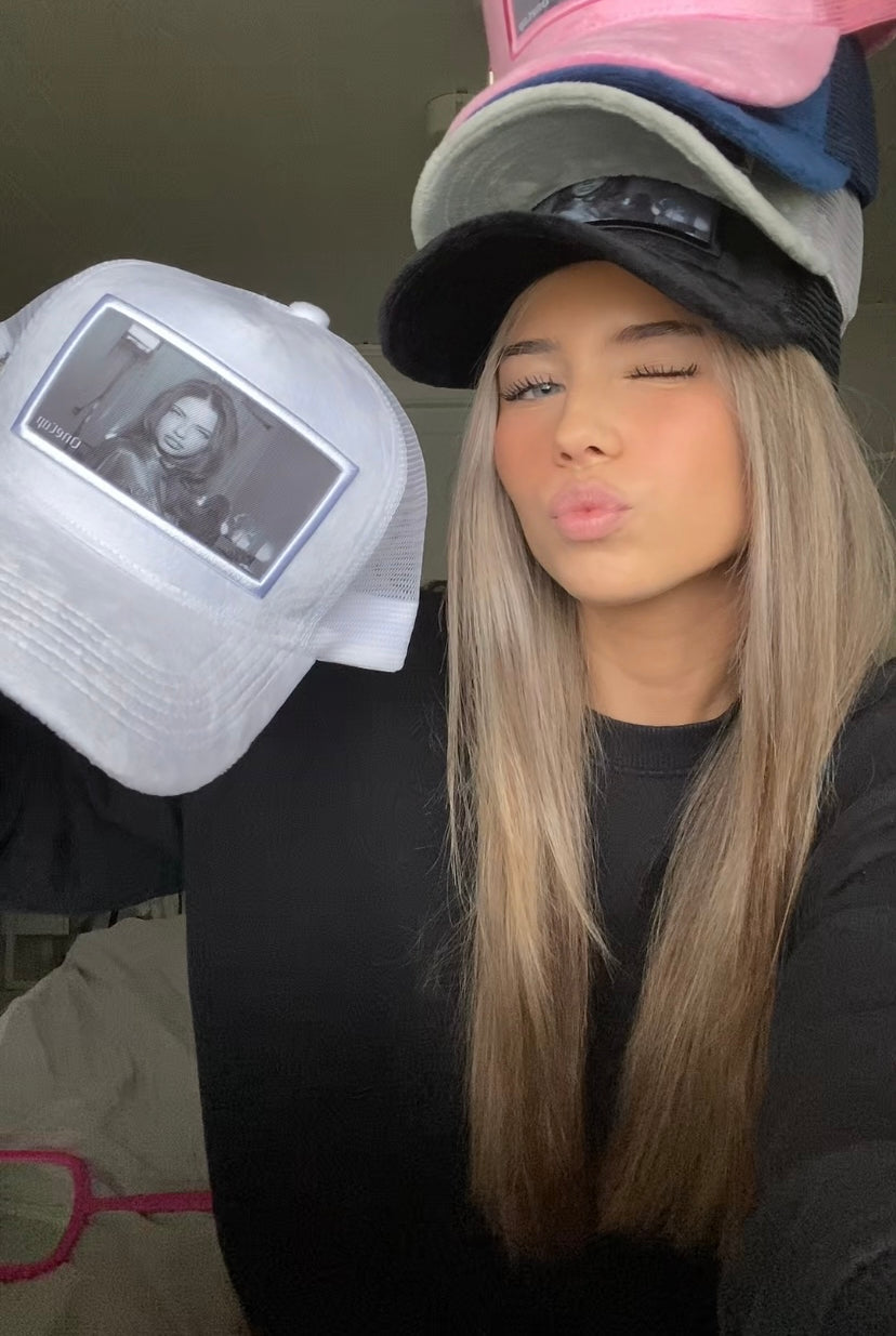 Woman wearing multiple hats with a printed image of Adriana Lima, displaying new hat collection.