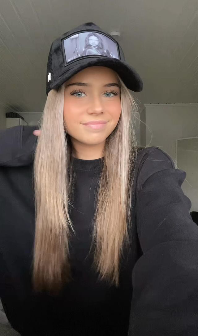 Woman with long blond hair wearing a black cap and black sweater smiles while posing indoors