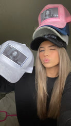 Woman wearing multiple hats with a printed image of Adriana Lima, displaying new hat collection.