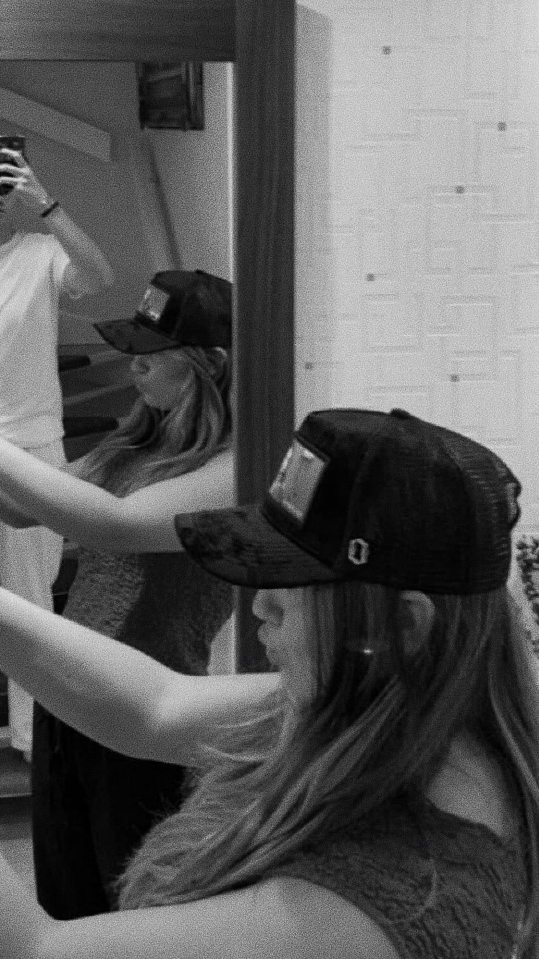 Woman in a black cap taking a mirror selfie in a modern, monochrome room.